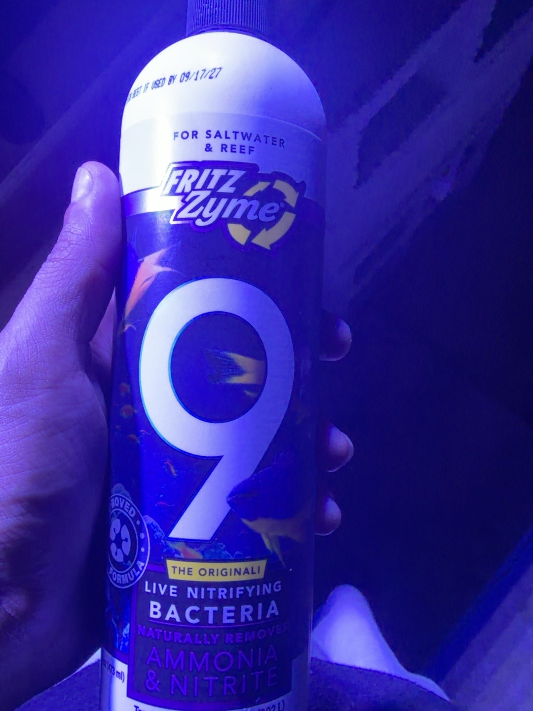 A bottle of Fritz nitrifying bacteria held beside the blue-lit trough
